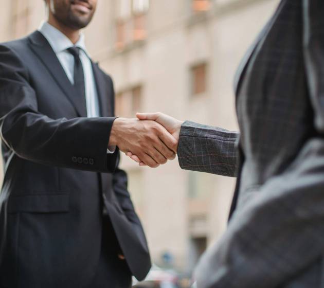 Dwóch osób w garniturach podających sobie ręce na tle miejskich budynków