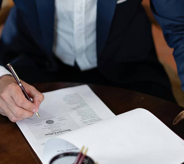 Mężczyzna w garniturze podpisujący dokument na biurku.