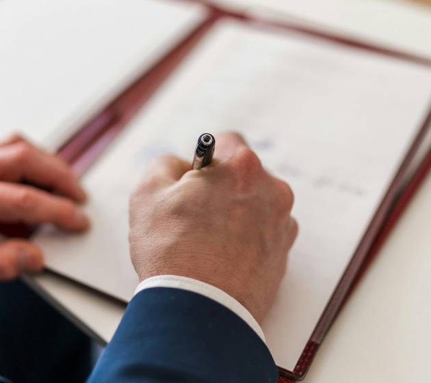 Mężczyzna w garniturze podpisujący dokument w teczce na biurku