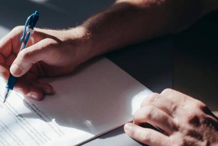 Zbliżenie na dłoń mężczyzny podpisującego dokument niebieskim długopisem