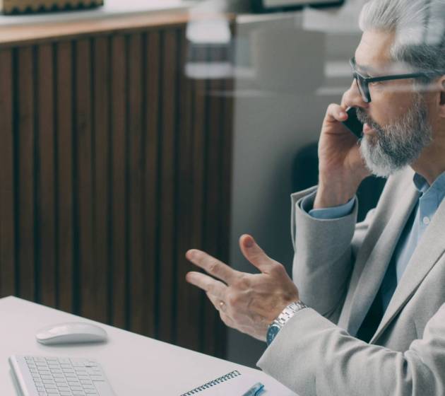 Biznesmen w okularach i marynarce gestykuluje podczas rozmowy przy biurku.